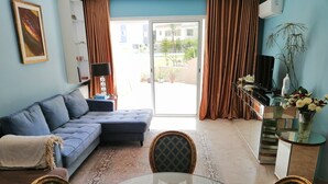 A living room with a blue sofa, a glass coffee table, and a dining area with chairs. - Superbe appartement avec Piscine (La Soukra)