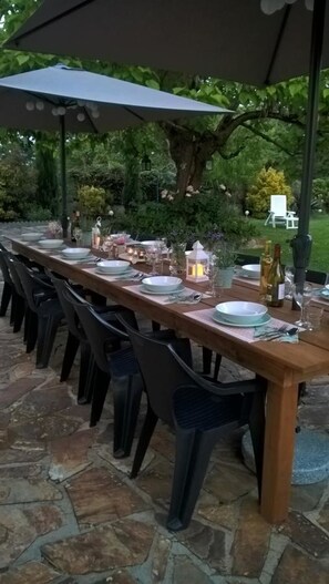 An outdoor dining area with a long wooden table set for a meal, surrounded by chairs, under a canopy. - La Maison Catalpa - Chambre d'hôtes (Saint-Privat-en-Périgord)