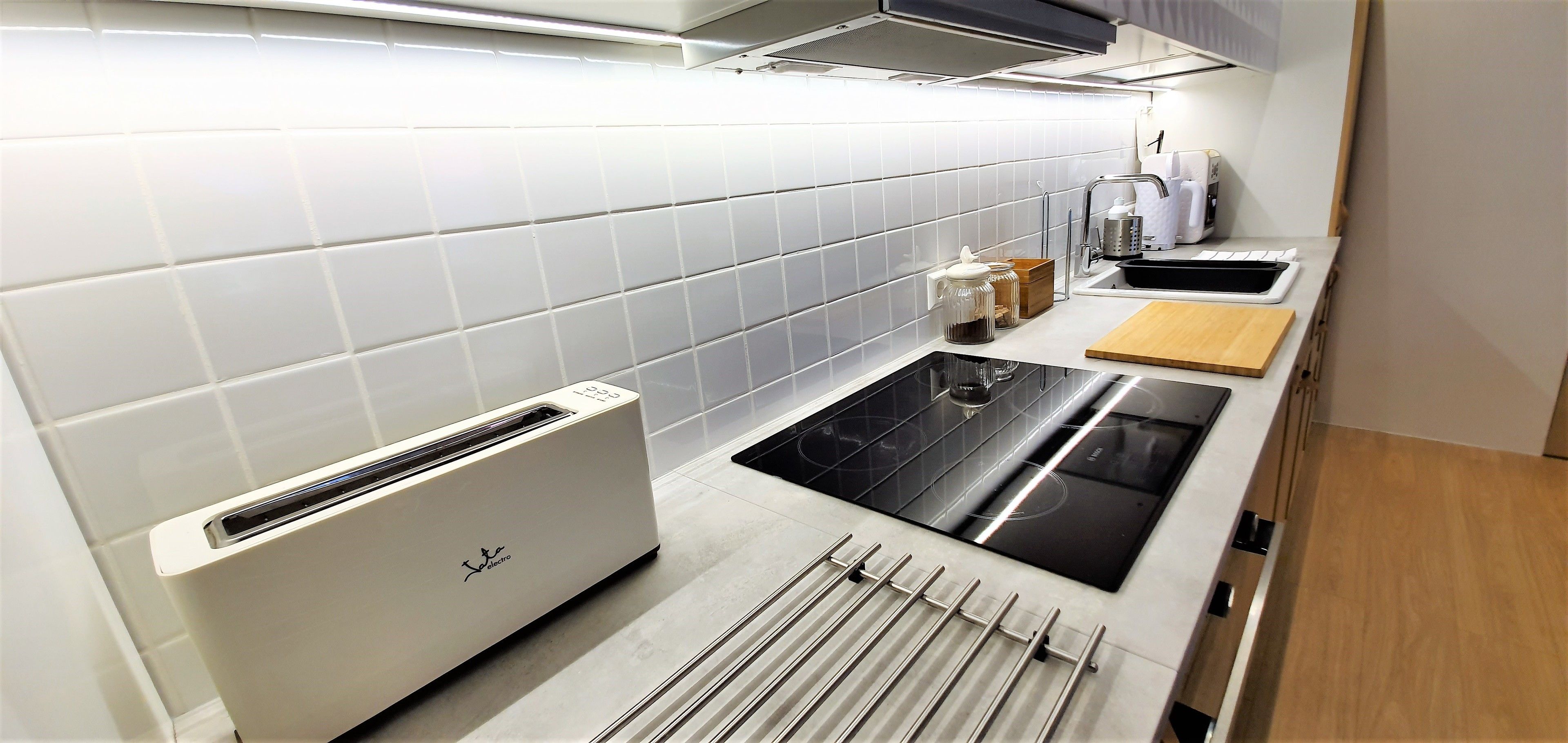 A modern kitchen with white tiles, a built-in toaster, a stove, and a wooden cutting board.