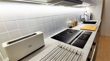 A modern kitchen with white tiles, a built-in toaster, a stove, and a wooden cutting board.