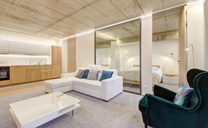 Un apartamento moderno con cocina, sala de estar con un sofá blanco y un sillón verde, y un dormitorio con cama y mesita de noche.