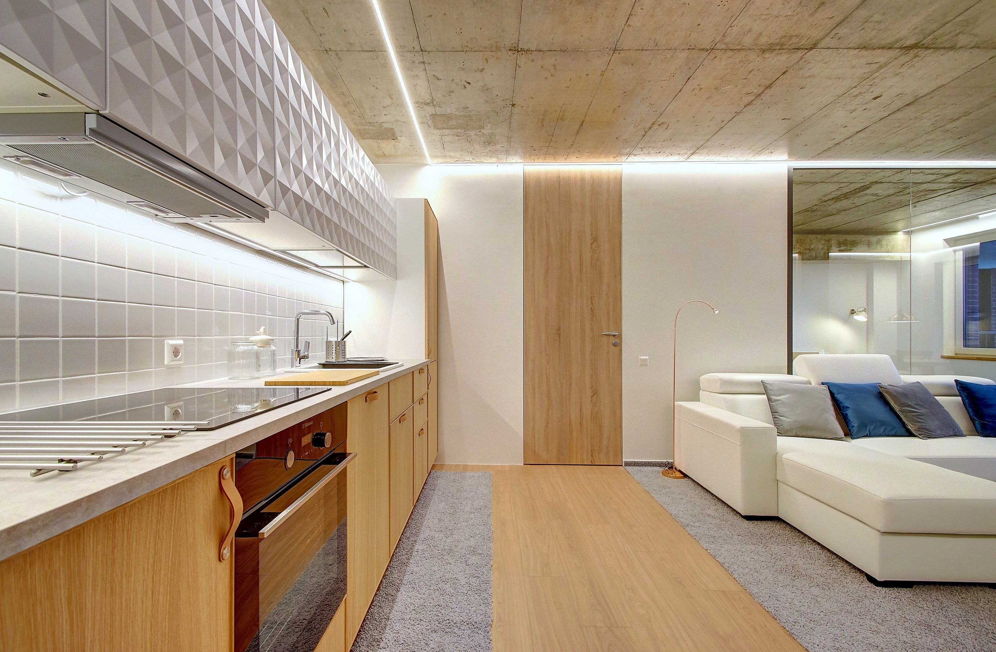 A modern kitchen with white tiles, wooden cabinets, and a built-in oven.