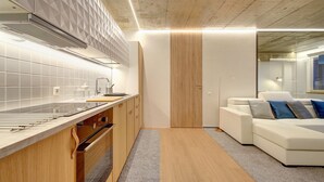 A modern kitchen with a wooden countertop, built-in cabinets, and a white backsplash. There is a white sofa with blue cushions in the adjacent living area. - Kauno-Algirdo Luxury Vilnius Apartments (Vilnius)