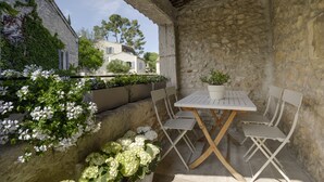 A stone patio with a white table and chairs, surrounded by white flowers and greenery. - Charming apartment in town house in the heart of Eygalieres (Eygalières)