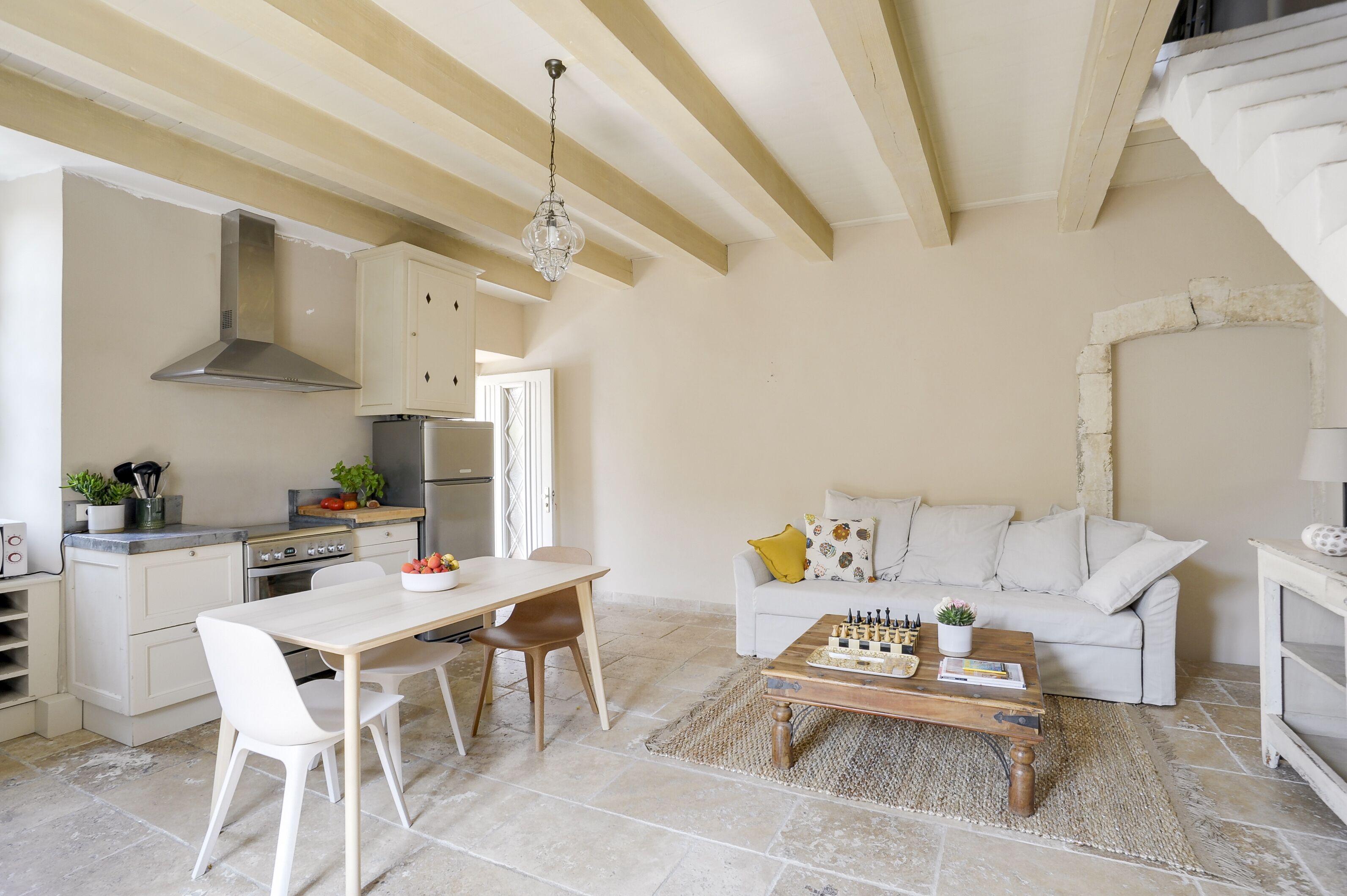Una cocina moderna con armarios blancos, una campana extractora de acero inoxidable y un comedor con mesa y sillas de madera.