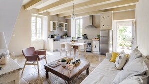 A spacious living area with a dining table, a sofa, and a coffee table. There is a kitchen in the background with cabinets and a refrigerator. - Charming apartment in town house in the heart of Eygalieres (Eygalières)