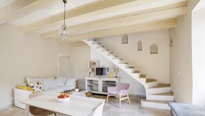 A spacious living area with a white sofa, a dining table, and a staircase leading to an upper level. - Charming apartment in town house in the heart of Eygalieres (Eygalières)