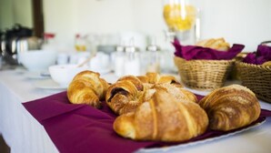 A breakfast table with croissants and baskets of bread, along with various breakfast items in the background.