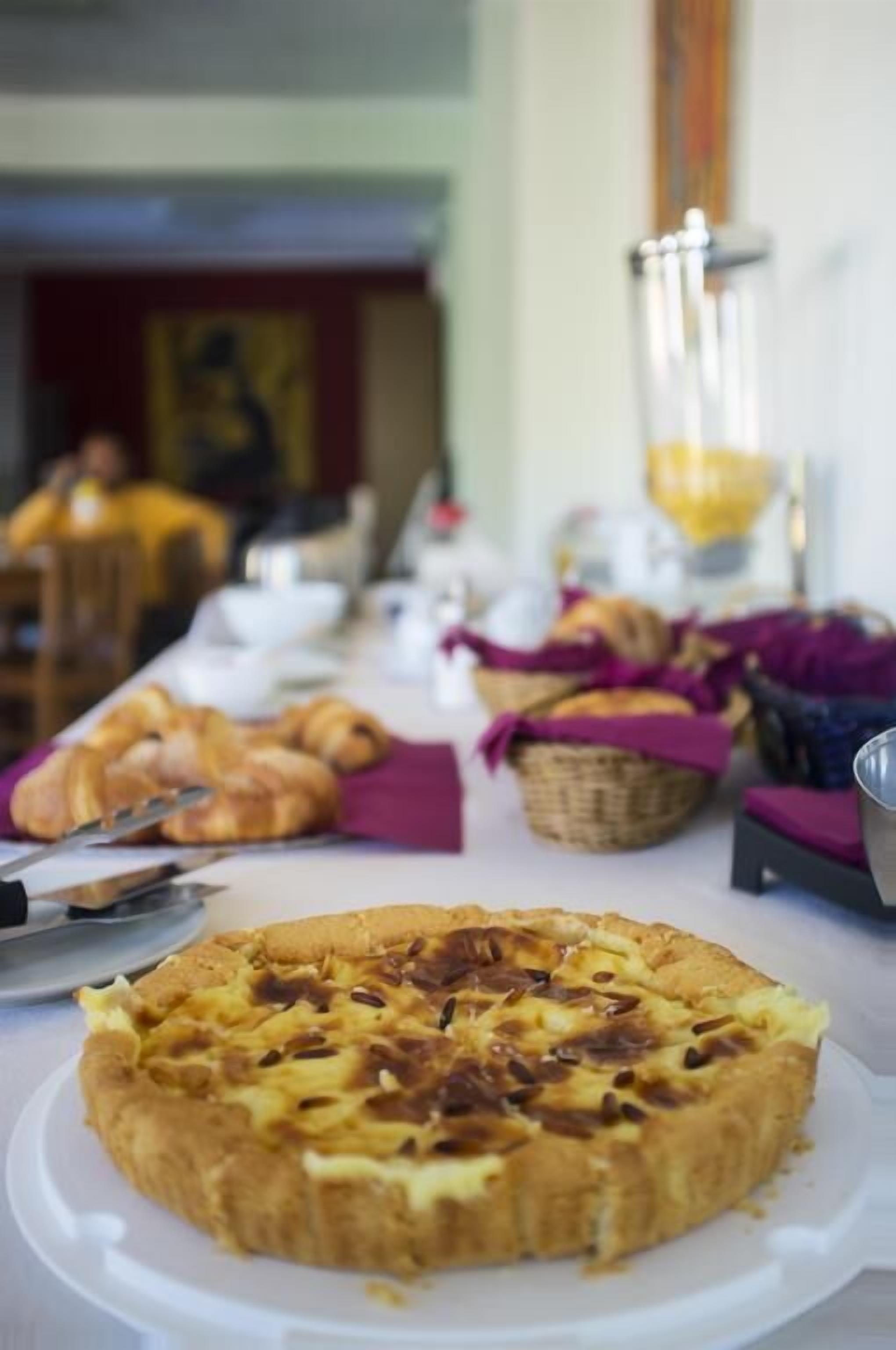 A buffet table with a variety of food items including a quiche and croissants.