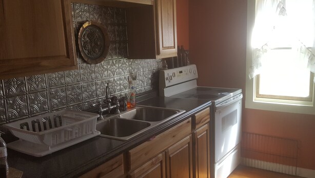 Una cocina con armarios de madera, un fregadero de acero inoxidable y una ventana con cortinas.