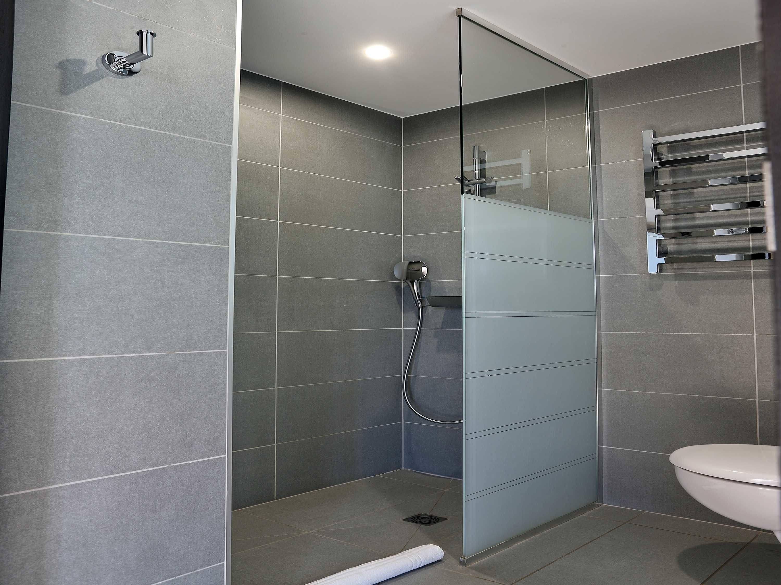 Una ducha moderna con puerta de vidrio, azulejos grises y un inodoro blanco.
