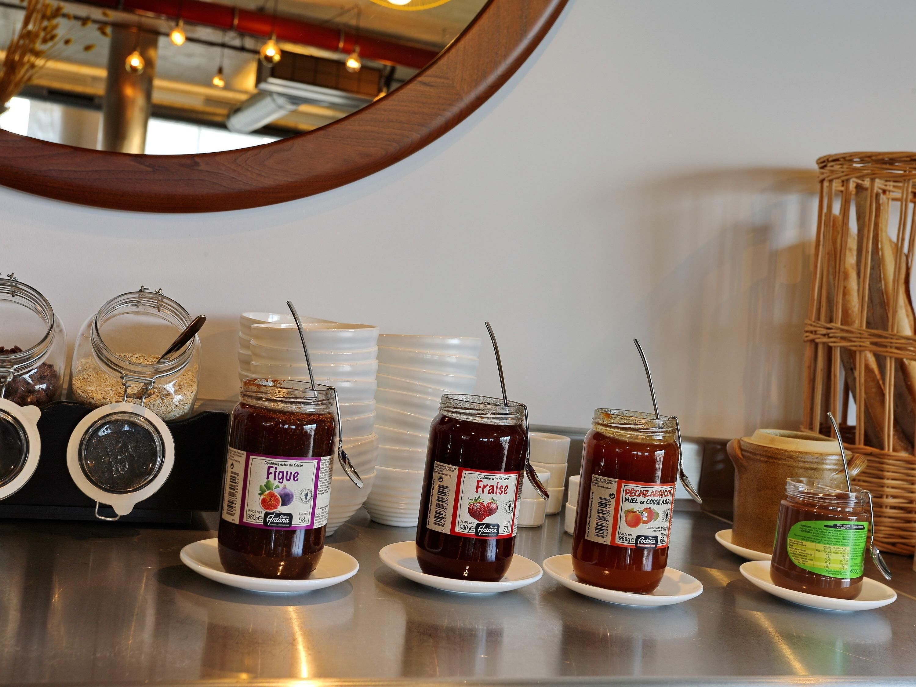 A display of various jars of jam on white plates, with a mirror reflecting the background.