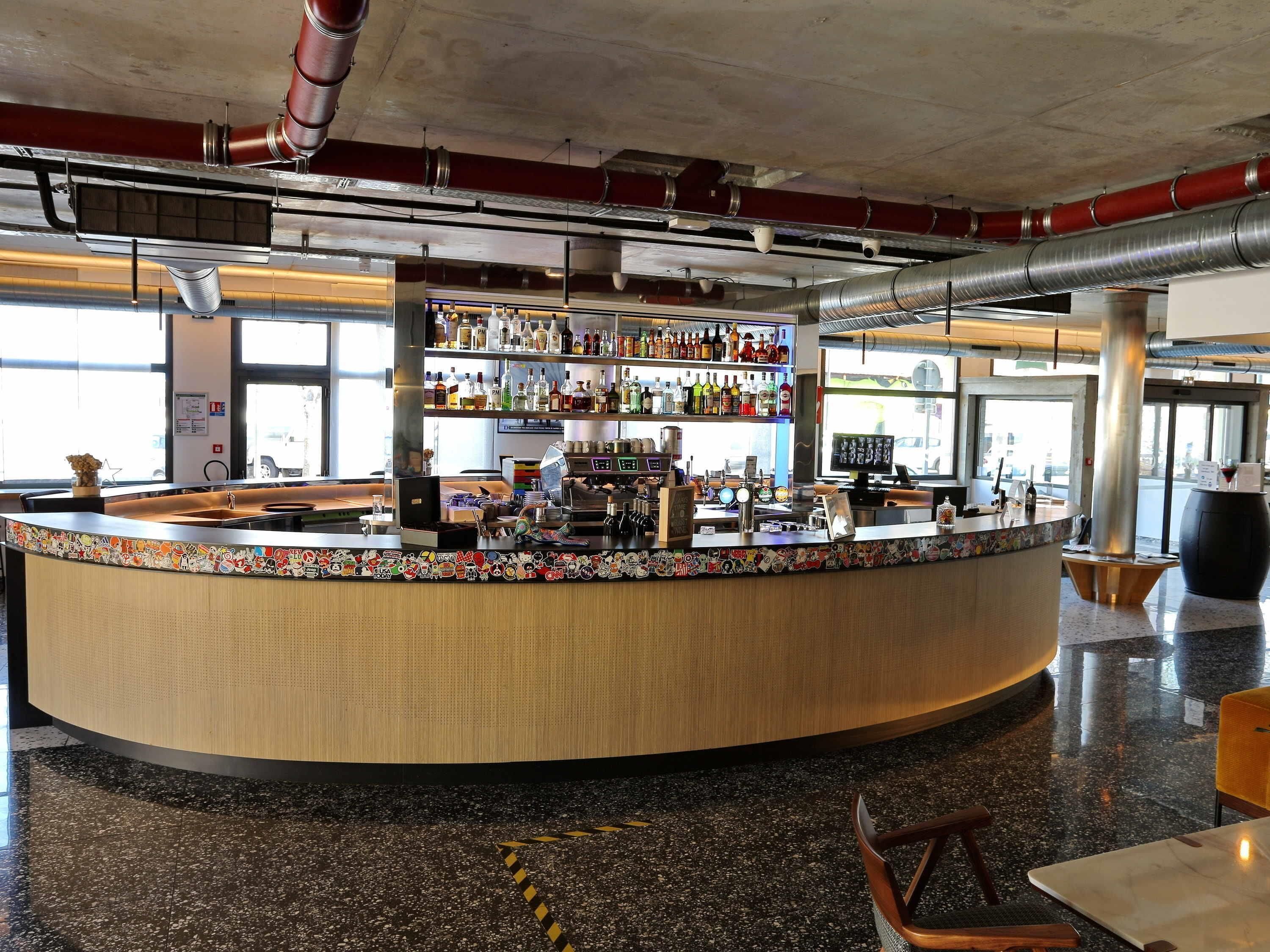A bar area with a curved counter, shelves with bottles, a coffee machine, and a large window.