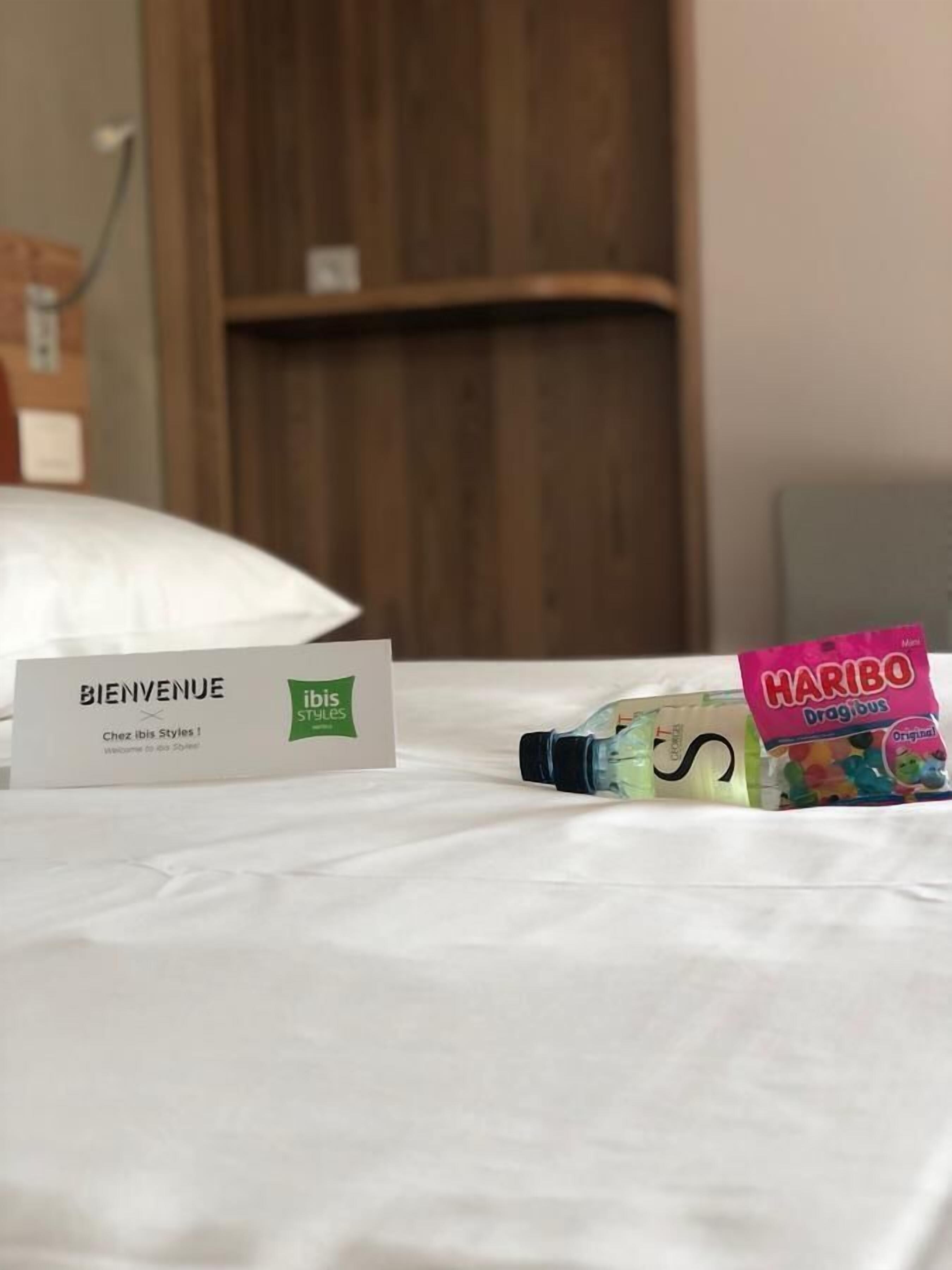 A hotel room with a welcome sign, a bottle of Haribo Dragibus, and a wooden wardrobe in the background.