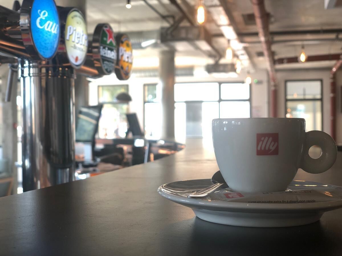 A coffee cup on a saucer with a logo, a beer tap with a blue label, and a beer tap with a yellow label.
