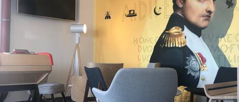 A modern room with a large flat-screen TV, a standing lamp, and a mural of a historical figure.