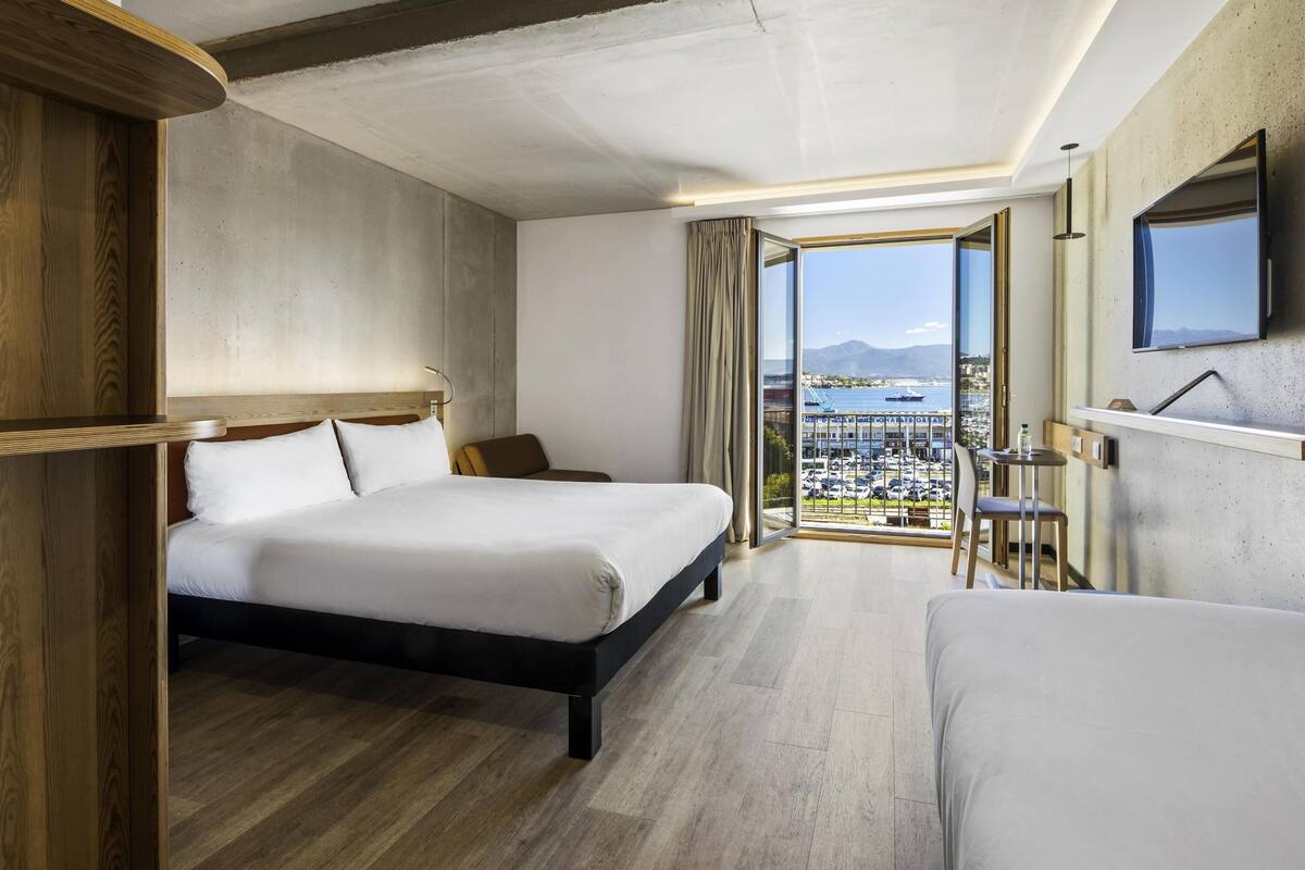 Une chambre d’hôtel avec un grand lit, un bureau, une chaise et une vue sur la ville et l’eau.