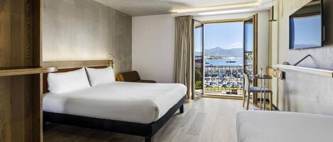 Habitación de hotel con una cama grande, un escritorio, una silla y vistas a la ciudad y al agua.