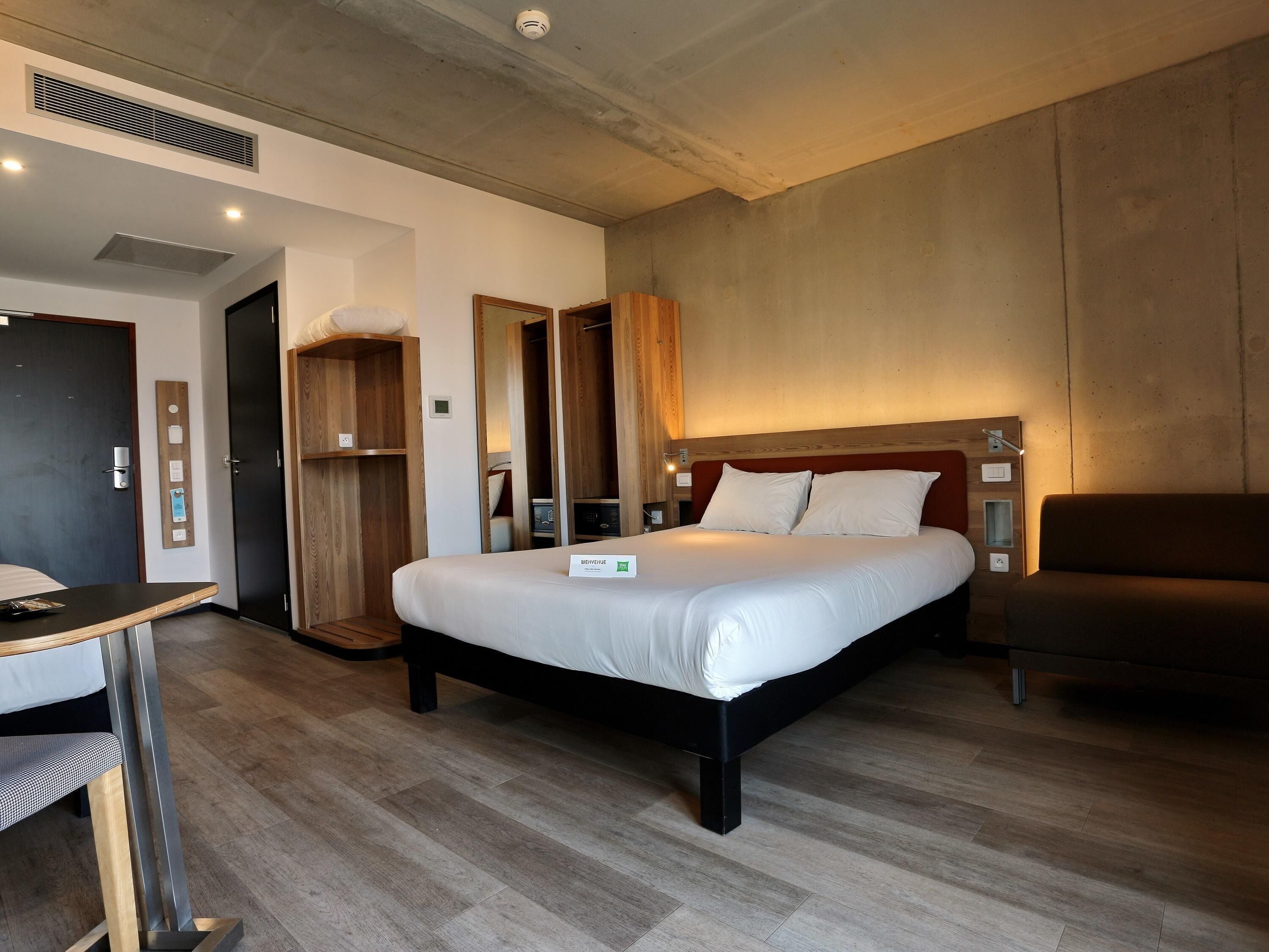 Una habitación de hotel con cama, escritorio, silla, armario y espejo.