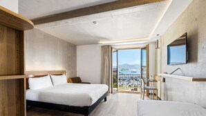 Ett hotellrum med en säng, ett skrivbord, en stol, en TV och ett stort fönster med utsikt över staden.