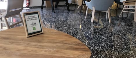 Un intérieur moderne avec une table en bois, des chaises, un sol noir à motifs et une affiche accrochée au mur.
