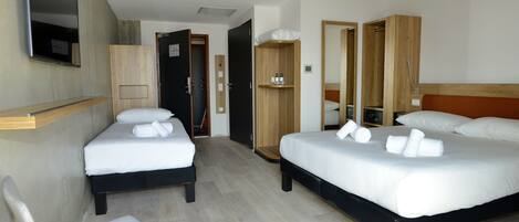 A hotel room with two beds, a chair, a wardrobe, and a mirror.