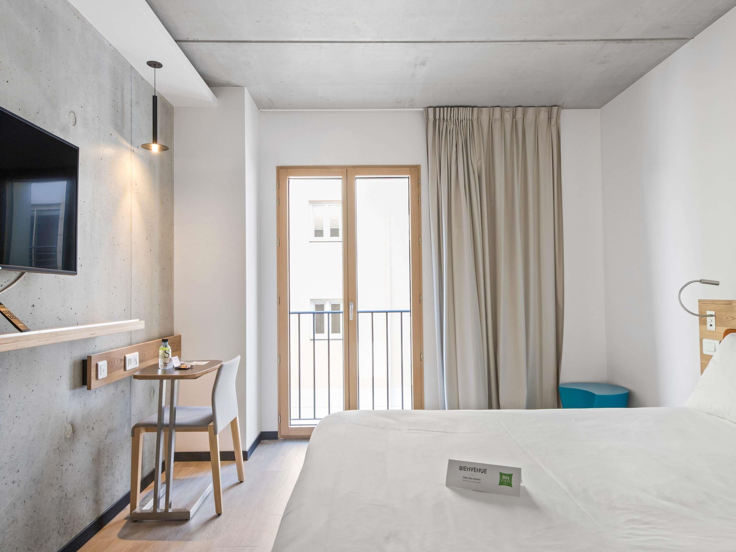 Habitación de hotel con cama, escritorio con silla, televisor y ventana con cortinas.