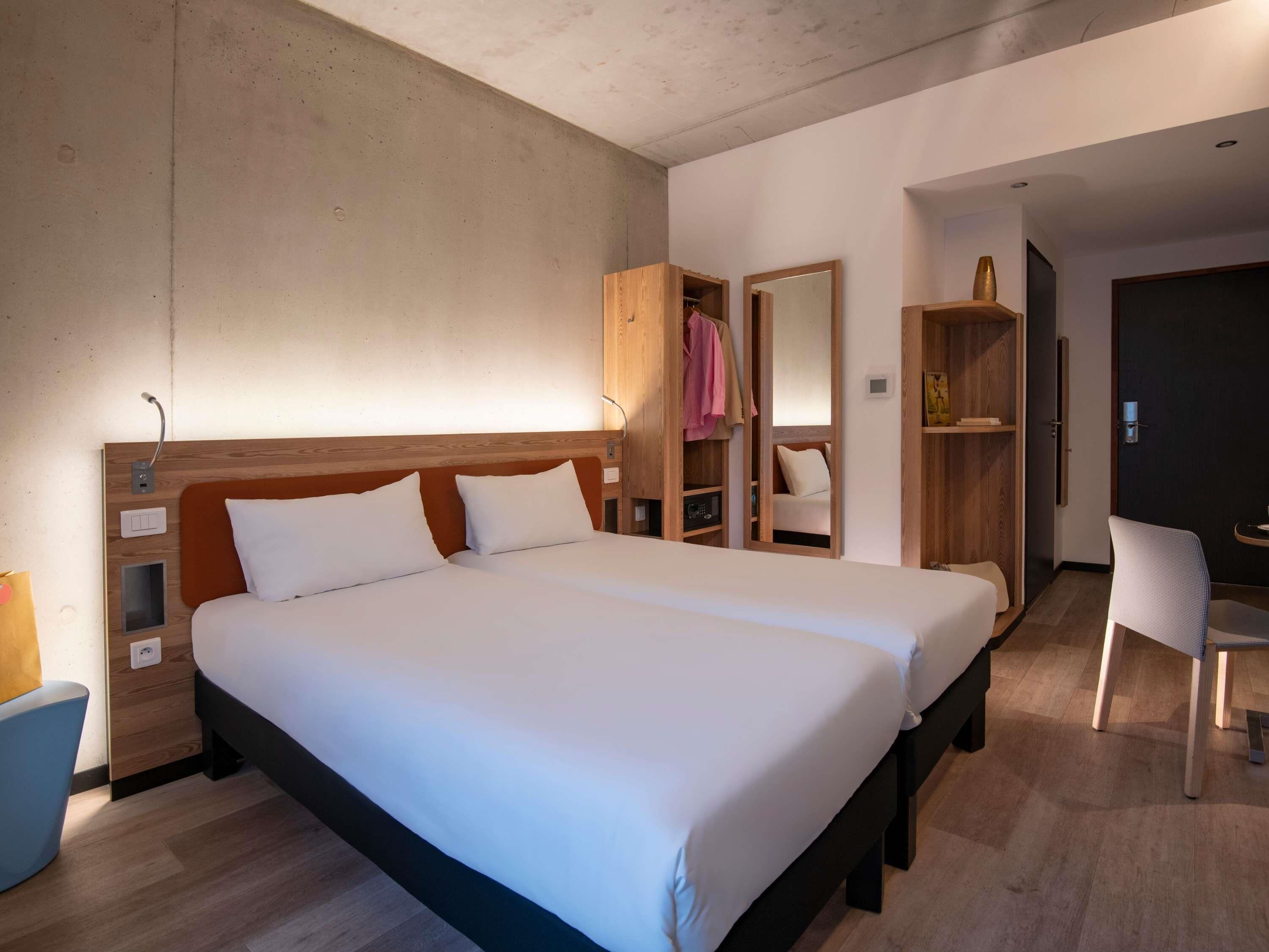 Una habitación de hotel moderna con una cama grande, un armario de madera, un espejo, un escritorio y una silla.