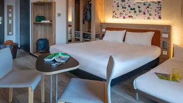 Habitación de hotel con cama, dos sillas, una mesita, armario y una pared decorada con un diseño.