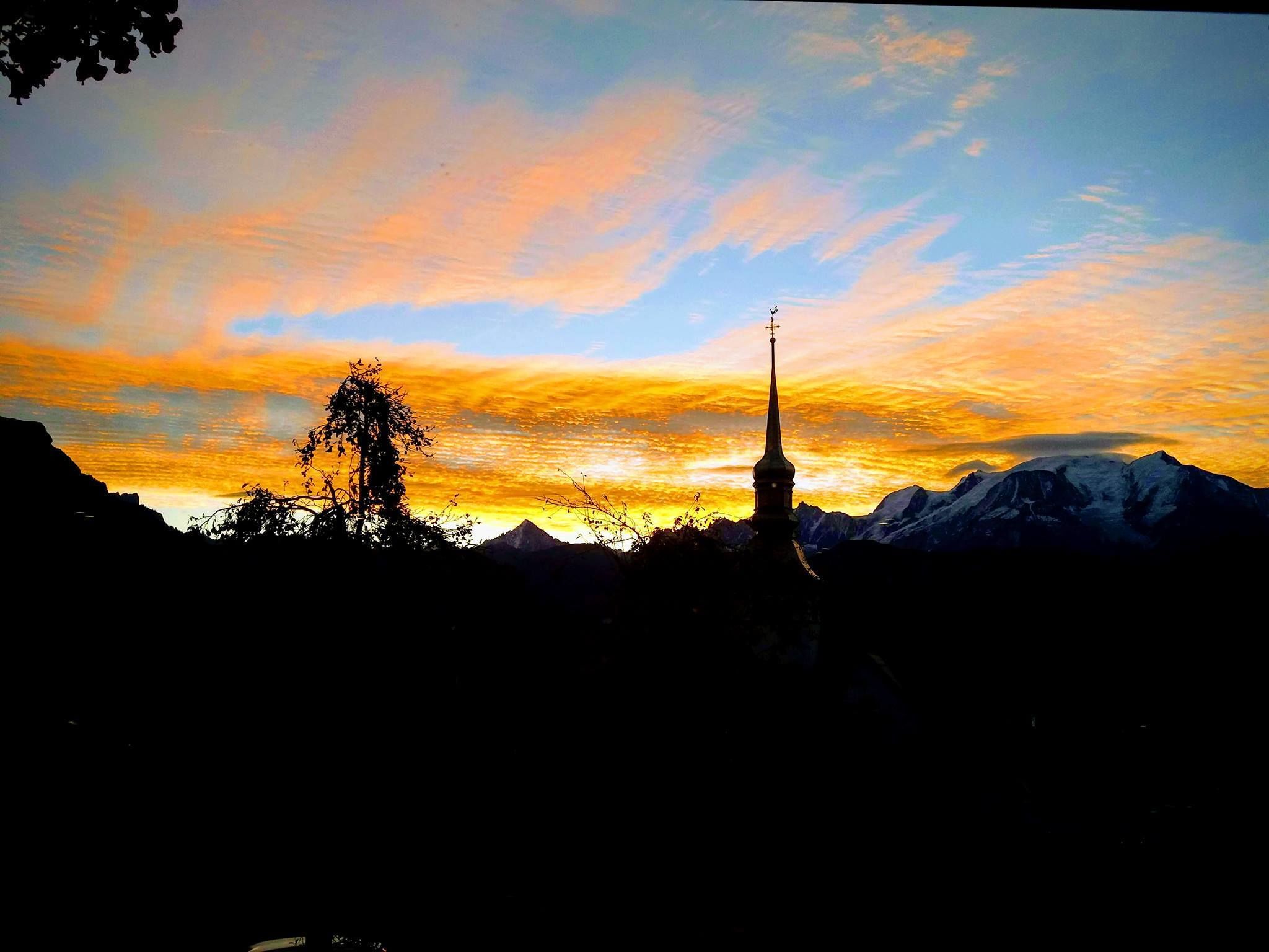 A mountain landscape with a church spire silhouetted against a sunset sky.