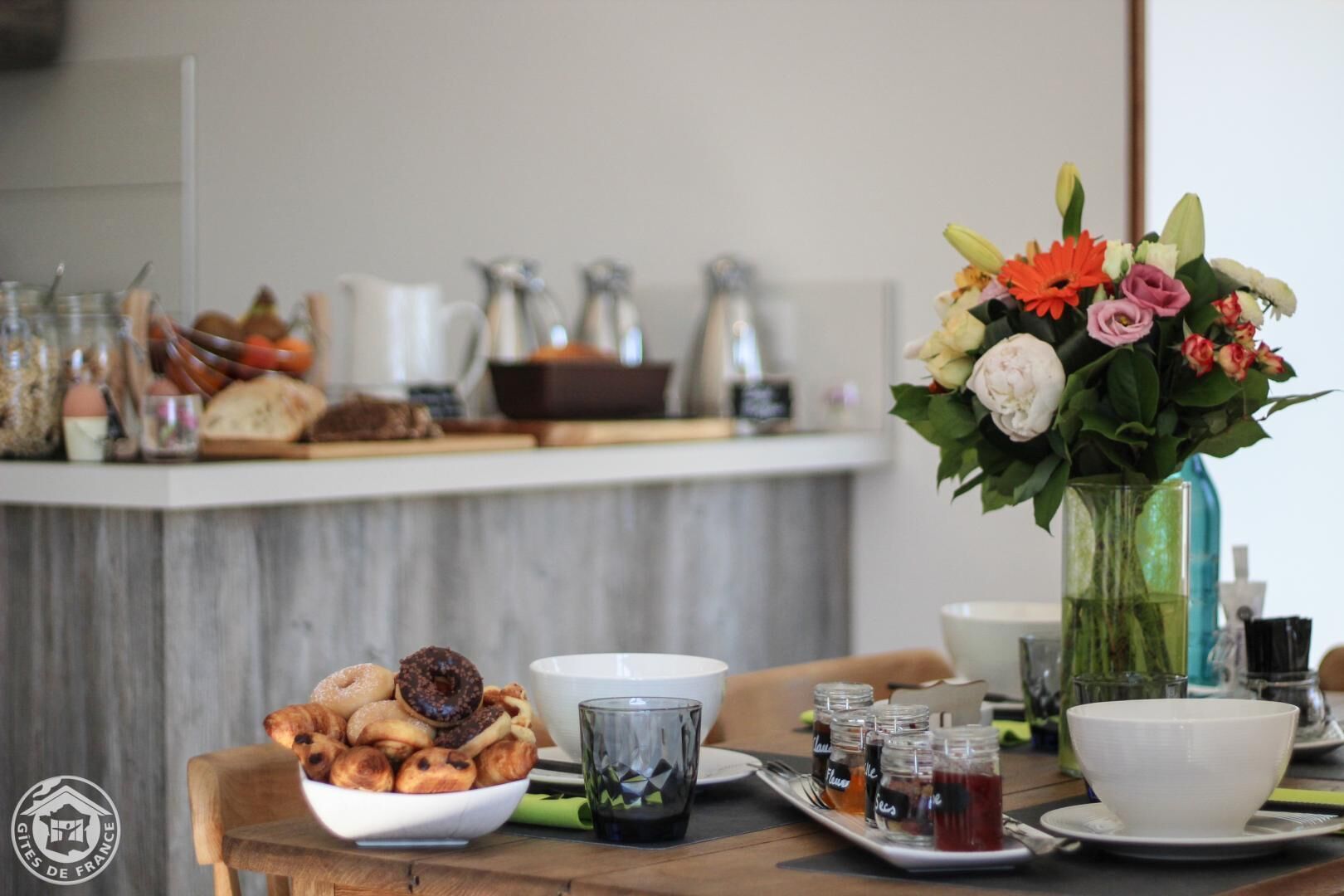 A breakfast setting with pastries, a vase of flowers, and a coffee station.