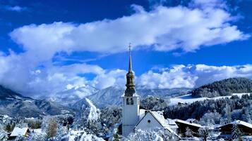 A snow-covered village with a church featuring a tall spire, surrounded by mountains and trees.