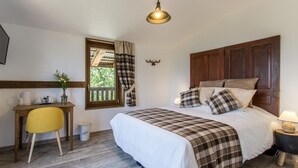 Un dormitorio con cama, escritorio, silla, ventana con cortinas, cabecera de madera y lámpara en una mesita de noche.