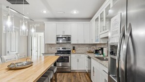 A modern kitchen with white cabinets, stainless steel appliances, a wooden dining table, and pendant lights.