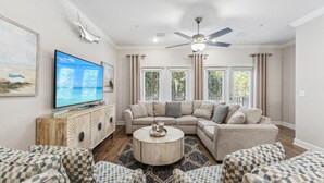 A living room with a sectional sofa, a round coffee table, and a flat-screen TV on a wooden cabinet.