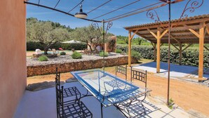 An outdoor patio with a glass table and chairs, a pergola, and a stone wall with plants. - Quiet country cottage with private pool (MORMOIRON)