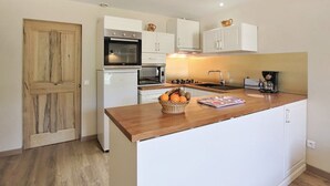 A compact kitchen with white cabinets, a wooden countertop, and a wooden door. - Quiet country cottage with private pool (MORMOIRON)
