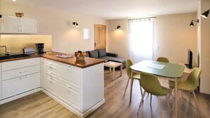 A modern kitchen with white cabinets, a wooden countertop, and a dining area with a green table and chairs. - Quiet country cottage with private pool (MORMOIRON)