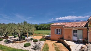 A house with a tiled roof, a small patio with outdoor furniture, and a garden with various plants and a gravel path. - Quiet country cottage with private pool (MORMOIRON)
