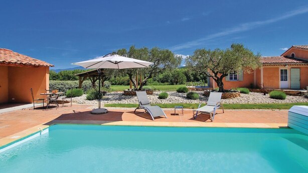 A swimming pool with lounge chairs and an umbrella, surrounded by a garden and a building with a tiled roof. - Quiet country cottage with private pool (MORMOIRON)