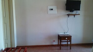 A room with a wooden bench, a small wooden table, a wall-mounted TV, and a power outlet. - Semo Hotel (Gumare)