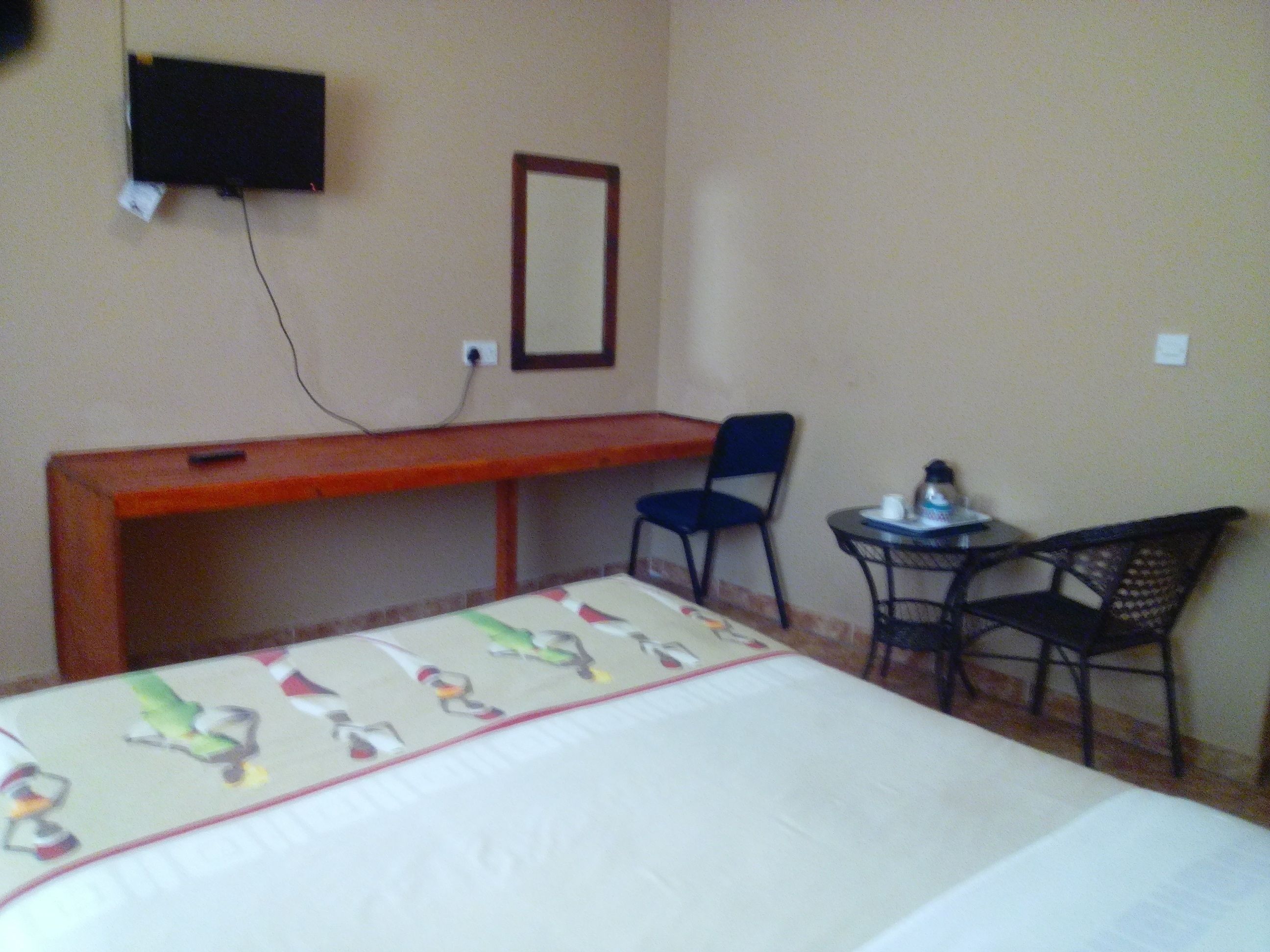 Une chambre d’hôtel équipée d’un lit, d’un bureau, d’une chaise, d’une petite table et d’un téléviseur fixé au mur.