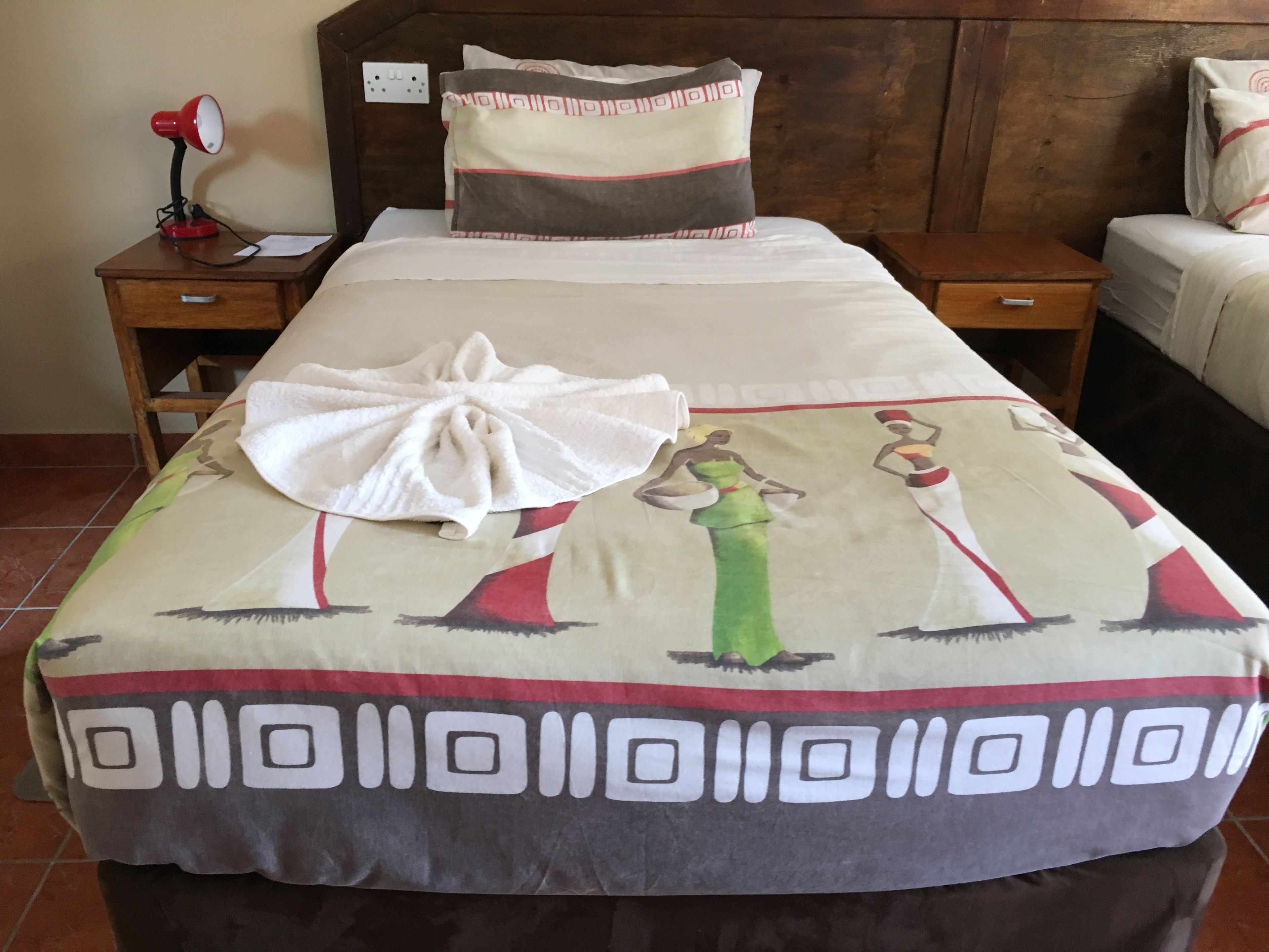 Una cama bien hecha con un edredón estampado, una lámpara de noche y una almohada con diseño geométrico.