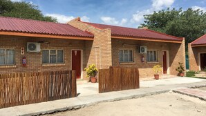 A row of brick buildings with red roofs, numbered doors, and fire extinguishers. - Semo Hotel (Gumare)