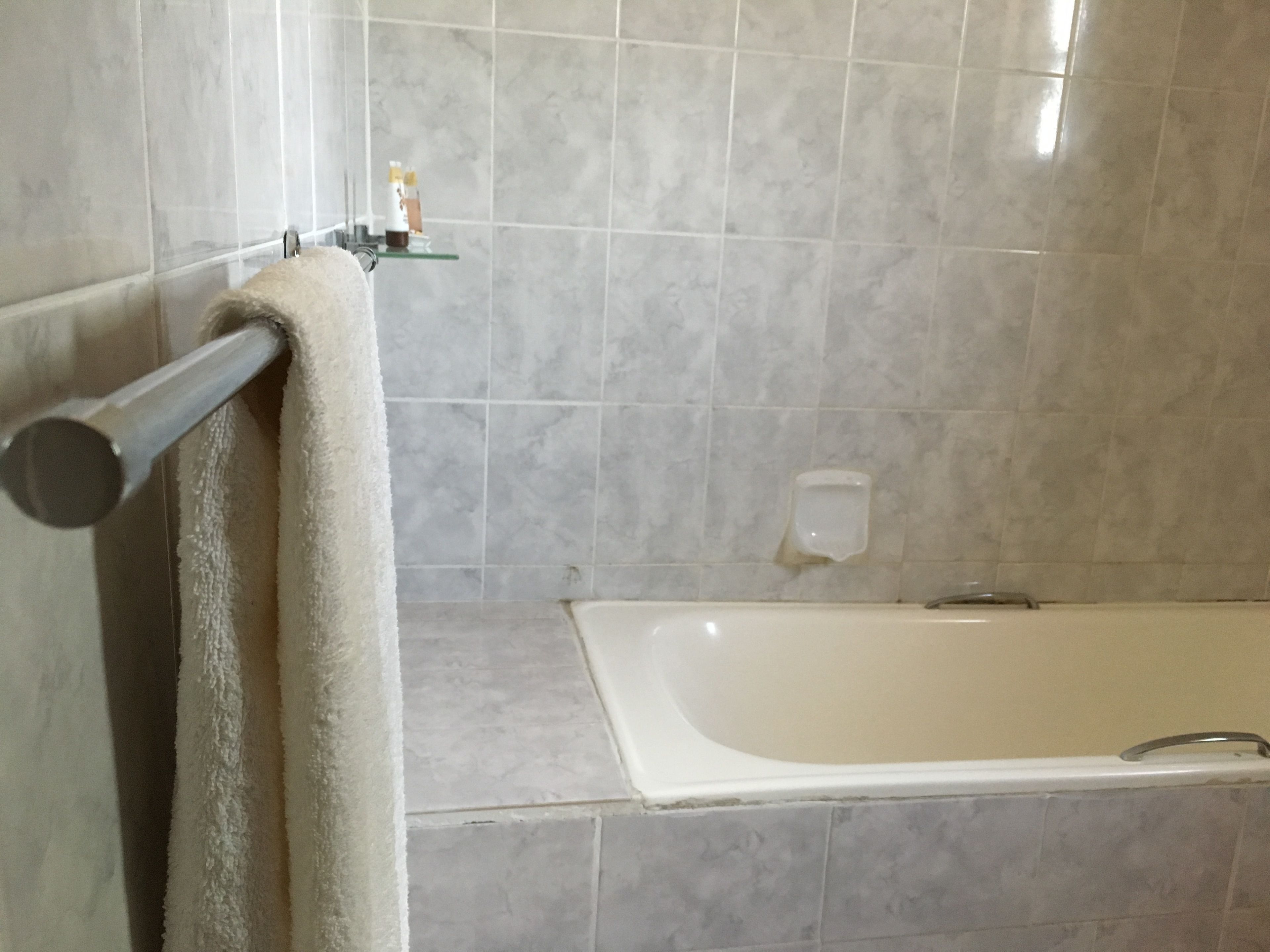 A bathroom with a bathtub, a towel rack, and a soap dispenser on the wall.