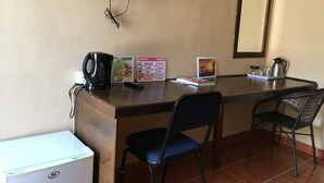 A small room with a desk, two chairs, a television mounted on the wall, a refrigerator, and a coffee maker. - Semo Hotel (Gumare)