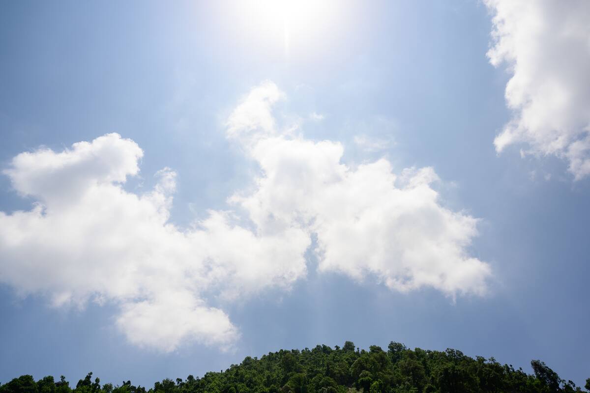 A clear sky with clouds and a forested hill.