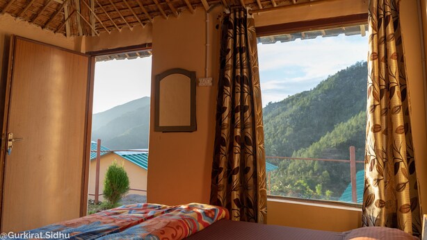 Una habitación con cama, ventana con cortinas, puerta de madera y vista a la montaña.