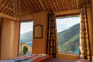 A room with a bed, a window with curtains, a wooden door, and a view of a mountain. - The Goat Village Escape (Nainital)