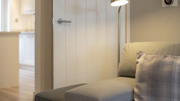 A modern living room with a sofa, a floor lamp, and a door leading to a kitchen.